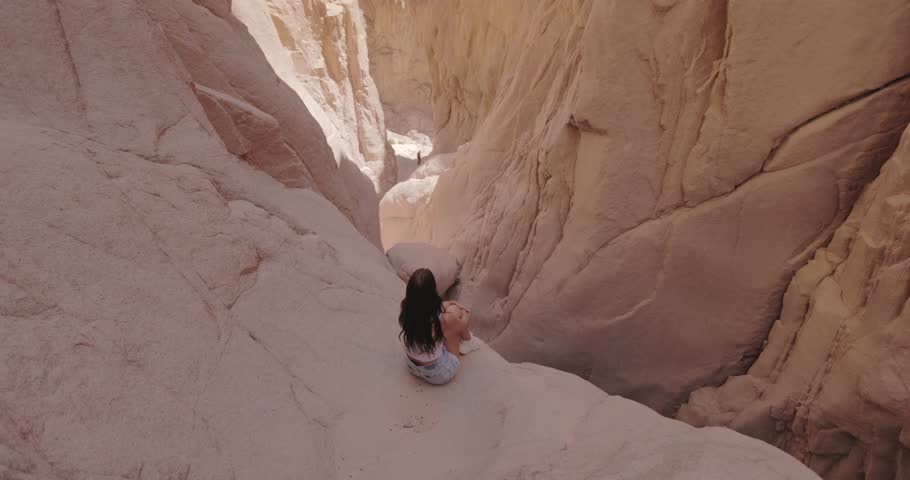 An epic tilt-up shot captures a woman sitting on a rocky ledge, enjoying the breathtaking view of Wishwashi Canyon in Egypt. Perfect for travel ads, adventure content, and nature exploration.