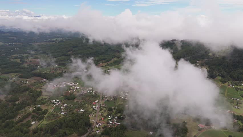 High above the sky, clouds drift over green forests and scattered villages, offering a peaceful view of nature and rural life.