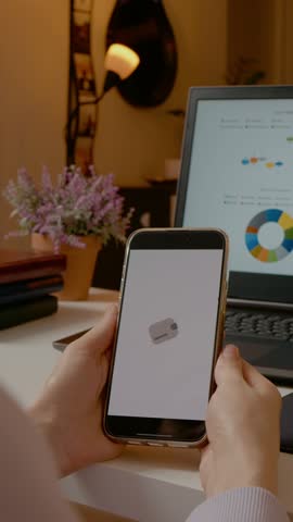 Vertical Screen: Businesswoman confirming online payment on smartphone with laptop showing graphs in background