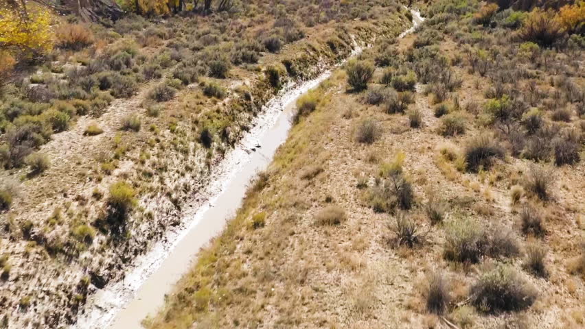 A narrow and winding river cutting through dry desert land surrounded by sparse autumn trees at Chaco Canyon, New Mexico.