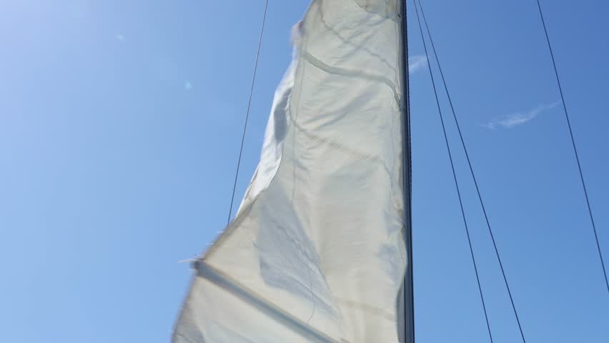 Sailing in the wind on sailboat with mast and sail. Open, unfurled white sails on a yacht against the blue sky