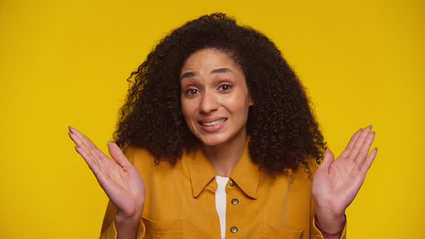 Playful Woman Shrugging with Awkward Smile on Yellow