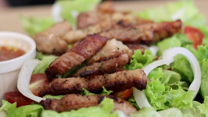 Close-up of grilled meat slices on fresh salad with a side of tangy dipping sauce.