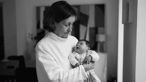 Grandmother holding baby newborn in arms by window standing at living-room home in artistic black and white. infant and grandparent together during first week of life - Powered by Shutterstock - Get 15% off with code: PIKWIZARD15