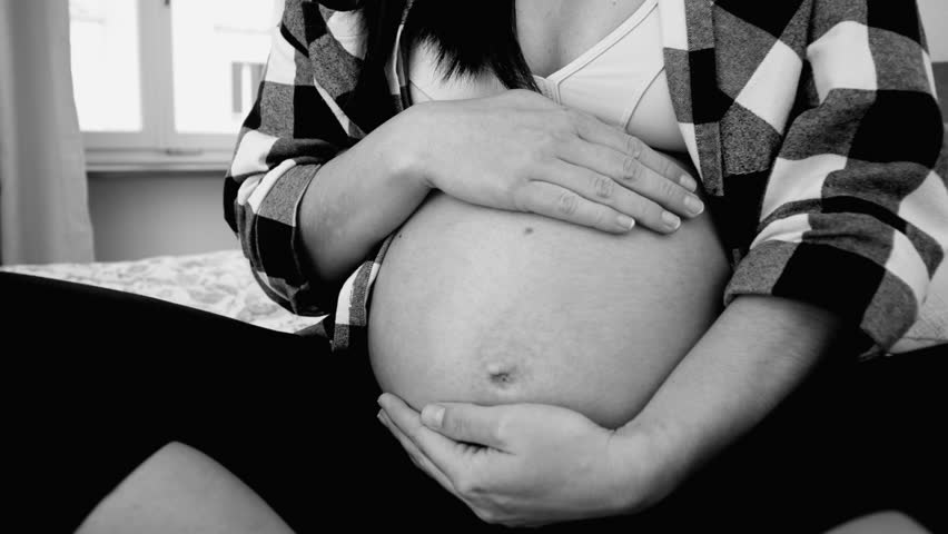 Close-Up of Pregnant Woman Caressing Belly, Tender Connection with Unborn Baby in Third Trimester in artistic black and white