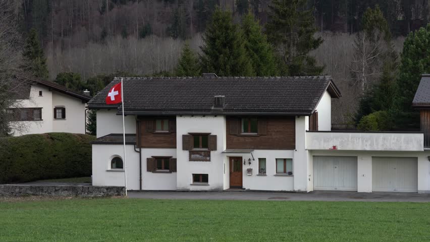 Swiss flag waving gently in the wind in front of a typical swiss house