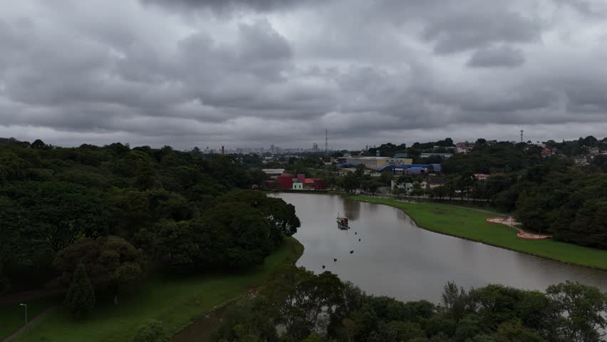 Curitiba, Paraná, Brazil - April 20 2025: Aerial drone footage over Parque São Lourenço and Belém River on a cloudy day, showing dense trees, green landscape, and urban nature scenery