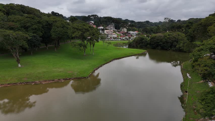 Curitiba, Paraná, Brazil - April 20 2025: Aerial drone footage over Parque São Lourenço and Belém River on a cloudy day, showing dense trees, green landscape, and urban nature scenery