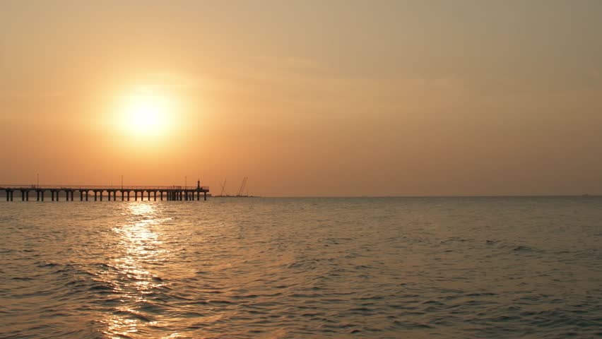 Silhouette of a pier in a seaport at sunset. Calm sea in the evening light. Empty space for text.