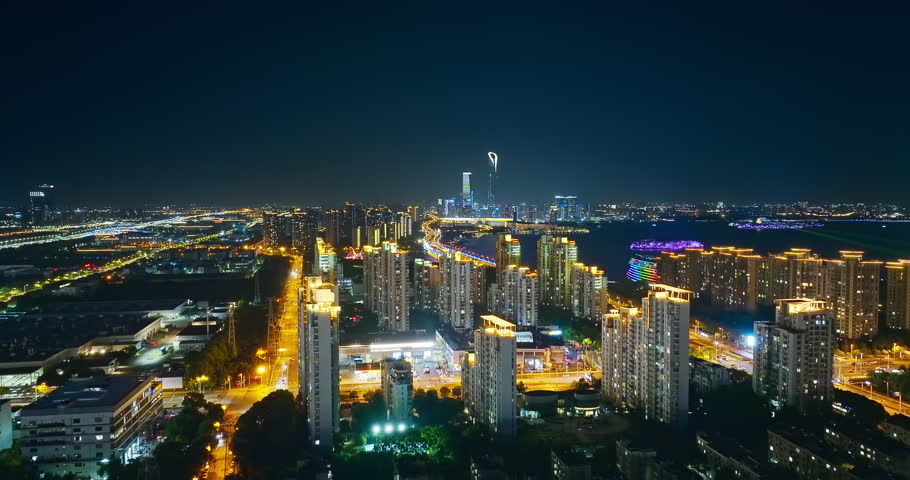 Aerial view of Suzhou cityscape with illuminated modern buildings and bridge over water at night.