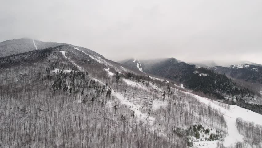 A rotating orbit drone shot over the gondola and ski lifts at Whiteface Mountain in the Adirondack Mountains, NY during light snow midwinter.