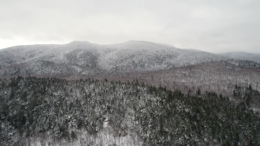 A snowy flyover drone shot of Stewart Mountain in the Adirondack Mountains in upstate New York, near High Peaks wilderness during midwinter in light snow.