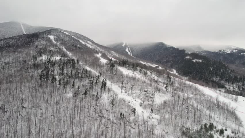 A receding, pulling away drone shot over the gondola and ski lifts at Whiteface Mountain in the Adirondack Mountains, NY during a light snow midwinter.