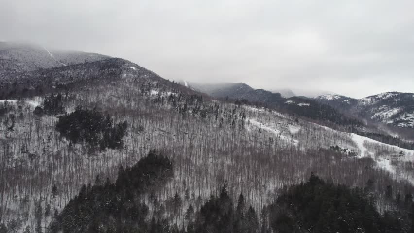 A slow rising drone shot with a dramatic low cloud ceiling shrouding the top of Whiteface Mountain in the Adirondacks, upstate NY during midwinter.