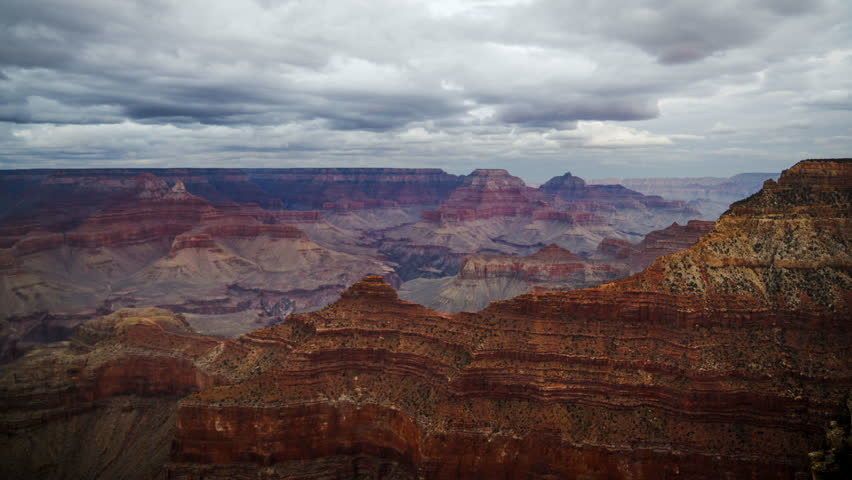 Grand Canyon with shifting light across the rocky landscape. Fast-moving clouds drift above. Time-lapse.