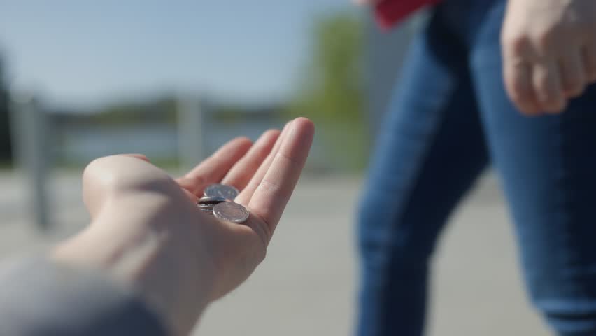 A close-up shot of a person placing coins into another person hand, symbolizing kindness, charity, and helping the homeless in a public outdoor setting.