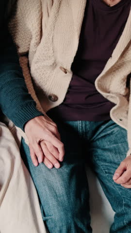 Vertical video, A gay couple sits together on a sofa, holding hands and sharing an intimate moment of affection. This clip portrays a sense of love, comfort, and togetherness.