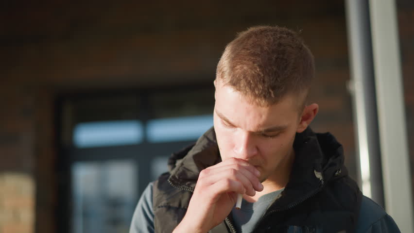 close up of young boy preparing to smoke pauses thoughtfully while holding cigarette then decides against it and throws it away with subtle expression of relief under soft natural light