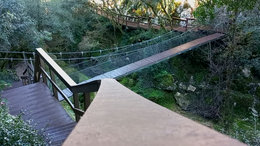Wooden walkways and a suspension bridge on the mountain slopes of the Mouros River Waterfall in Condeixa-a-Nova, Portugal, a fantastic trail surrounded by nature in shades of green and brown.