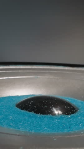 Loudspeaker plays music and throws blue hydrophobic sand upward. Colored aquarium sand moves depending on intensity of sound waves. Demonstration of acoustic system operation macro