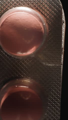 Curved silver blister with pink pills on black background. Effective painkillers prescribed by doctor from headache symptoms. Pharmacy concept macro