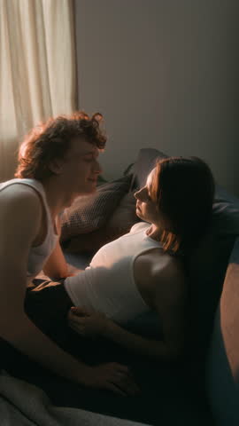 Vertical shot of intimate moment between affectionate couple, hugging and nose bumping on couch
