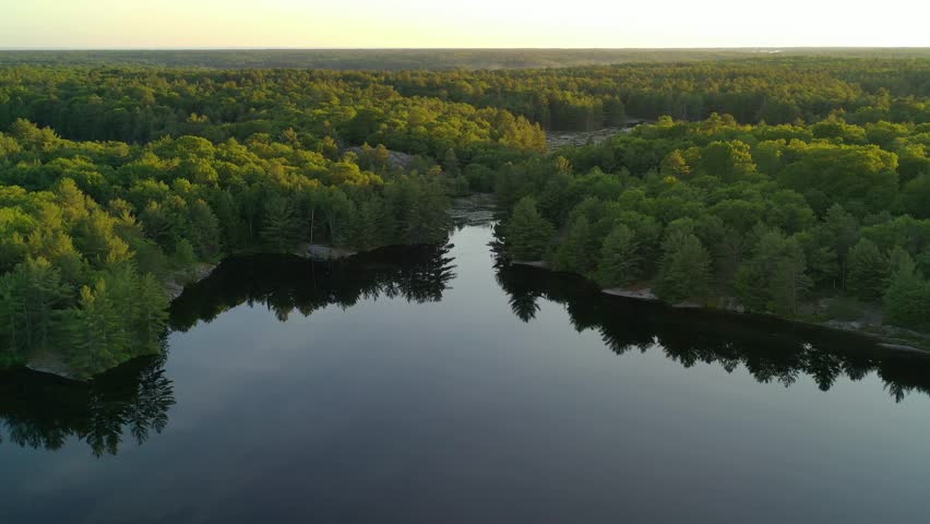 Aerial view flying over calm reflecting lakes, vast forests and swamps in rural Ontario at sunset.