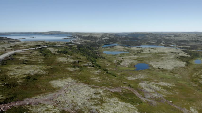 Scenic aerial shot of wild northern nature in Teriberka, Russia. Rocky tundra, lakes and distant Barents Sea horizon under clear blue sky
