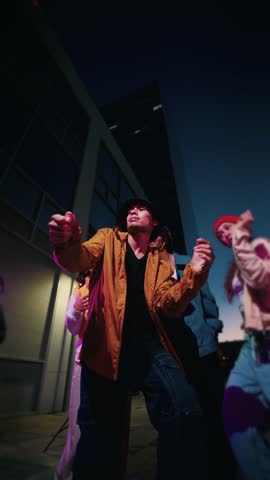 Vertical. Dancing young people breakdancing in street hip hop dancer practicing dance routine performing freestyle moves in city at night. Urban style friends rap music