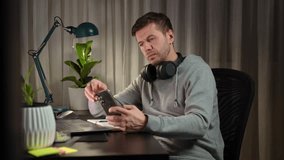 Tired freelancer procrastinating at home office, scrolling phone instead of working. Unproductive man using smartphone at home desk. Concept of procrastination and distraction in remote work - Powered by Shutterstock - Get 15% off with code: PIKWIZARD15