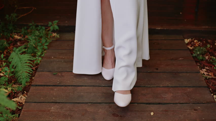Dynamic close-up of a bride walking toward the camera on a wooden deck. The elegant movement and texture of the wood create a natural, cinematic wedding detail.