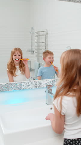 Two kids, brother and sister, standing side by side in bathroom brushing teeth in front of mirror. Morning routine boy girl emphasizes health, discipline, and proper dental hygiene in everyday life.