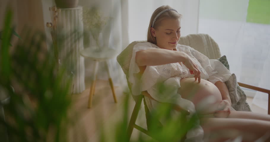 A joyful expectant mother at an advanced stage of pregnancy enjoys time with her child, tenderly touching and embracing her bump.