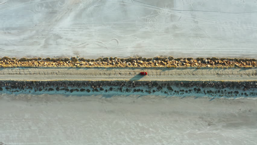 This overhead drone tracking shot dramatically highlights a bright red vehicle cruising across the endless white plains of Salt Lake.