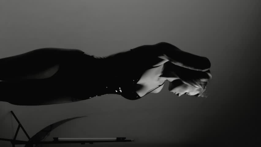 Blonde with a beautiful figure in a black patent leather bodysuit posing in a studio. Studio lighting, low exposure, monochrome image