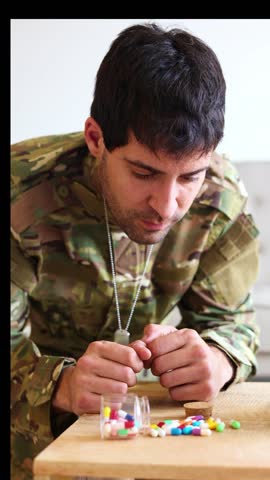 vertical Military veteran wearing camouflage uniform sitting at home, struggling with post-traumatic stress disorder, consuming medication for managing anxiety and depression symptoms
