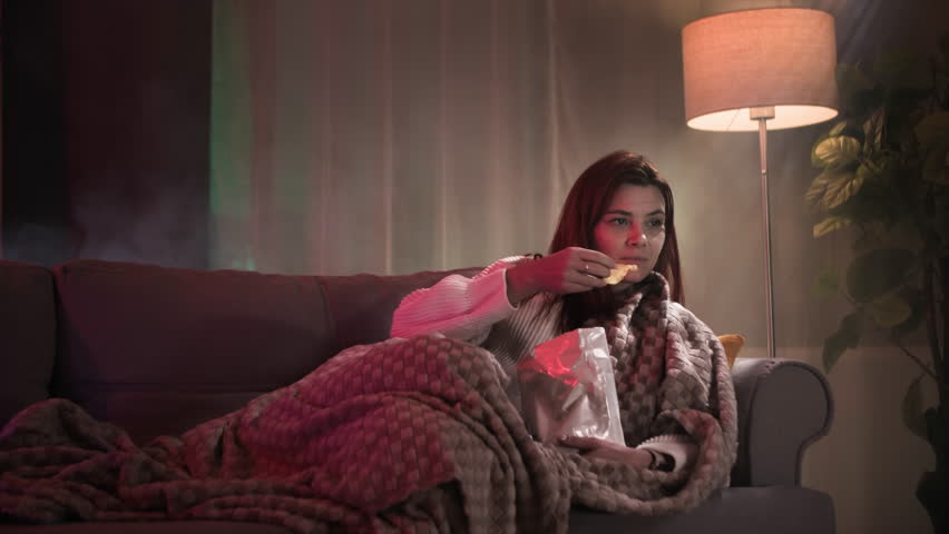 beautiful redhead woman eating potato chips and watching TV series in dark room