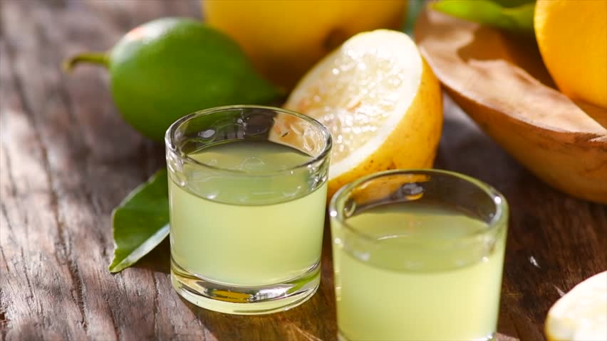 Limoncello, Italian liqueur with lemons. Traditional Mediterranean sweet shot alcoholic drink close up, little glasses and fresh citrus fruits on wooden table. Lemon juice 