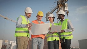 Engineers analyzing blueprints, discussing designs, using laptop, rooftop with cranes nearby. Team of multiethnic men and woman reviewing plans, coordinating, collaborating on rooftop of construction. - Powered by Shutterstock - Get 15% off with code: PIKWIZARD15
