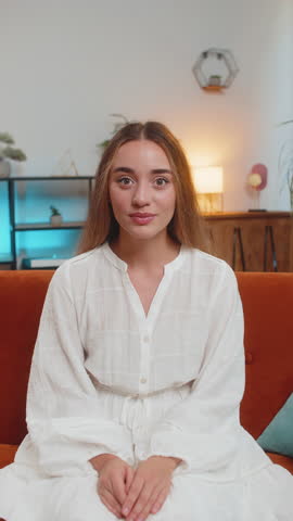 Oh my God, Wow. Young woman surprised looking at camera with big eyes, shocked by sudden victory, good win news, celebrating at home. Excited amazed girl indoors in living room on couch. Vertical