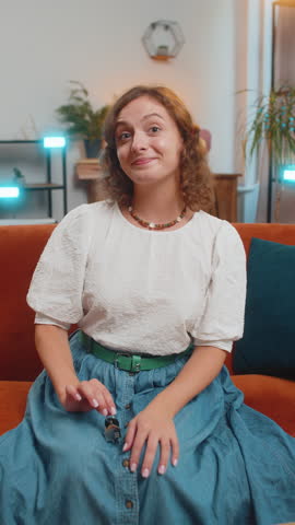 Happy young woman real estate agent lifting hand showing the keys of new home house apartment, buying or renting property, mortgage loan at home indoors. Girl sitting on orange sofa couch. Vertical.