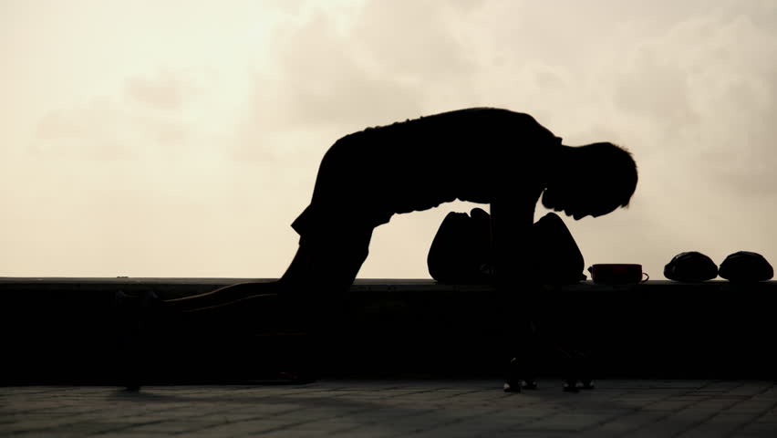 Soft unrecognizable silhouette of the man exercising at sunrise, morning physical activity.