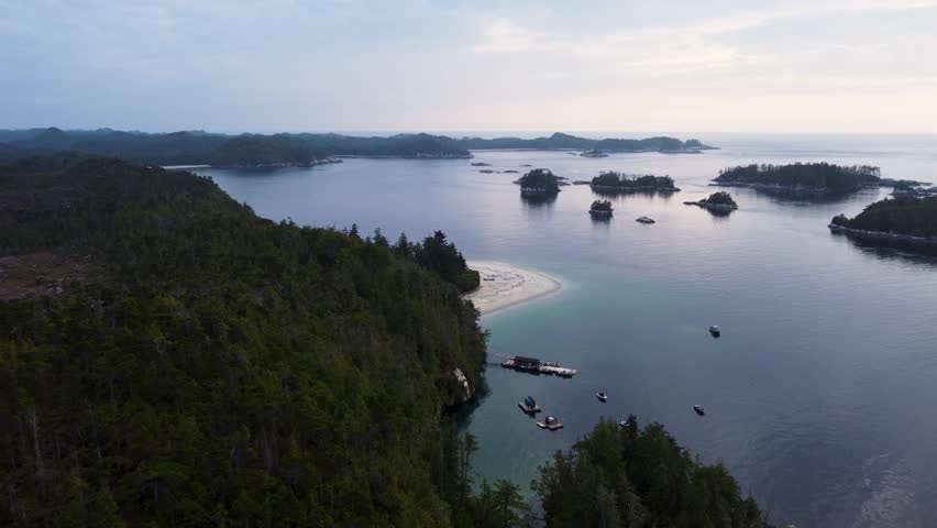 Aerial view over Calvert Island, British Columbia. Flying towards a solitary beach, a dock and boats moored below