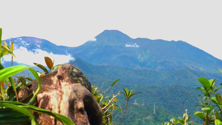Scenic view of lush green mountains and forested hills under a cloudy sky, captured in West Java, Indonesia.