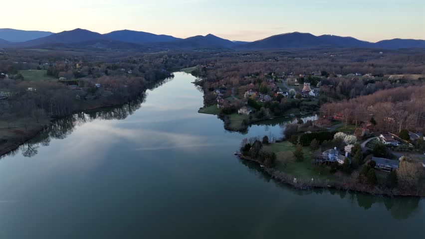 Tranquil James River during sunset time in Virginia, USA. Aerial wide shot. Mountain range in background. Houses and villas in luxury district of american town at dusk. Spring season in America.