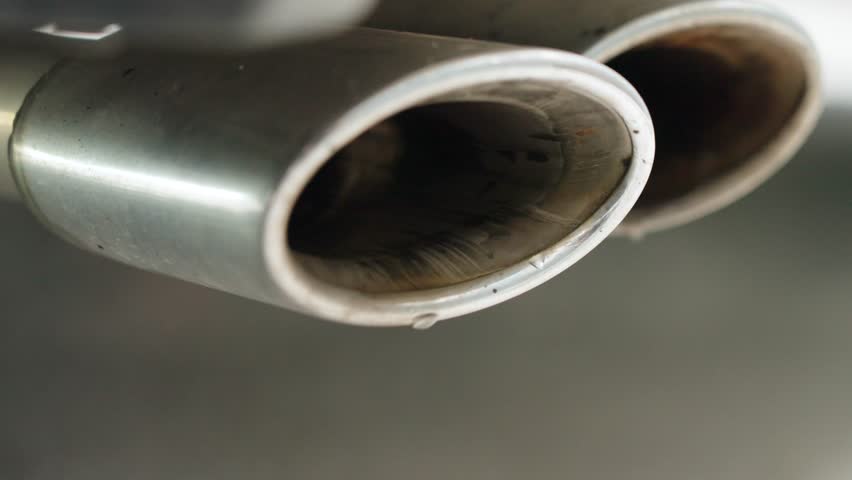 Close-up of a V8 double exhaust with water vapor droplets bursting out. Powerful cinematic shot emphasizing engine force and motion.