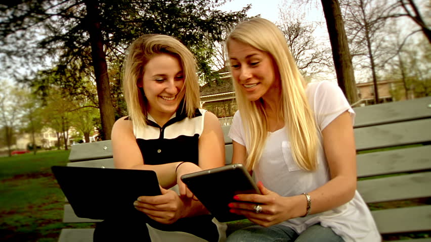 Two young women enjoy using their tablet PCs in the park.
