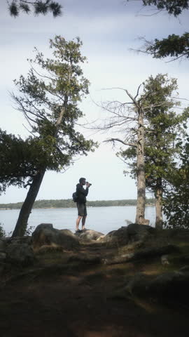Vertical shot of a photographer capturing nature at Wellesley Island State Park in Fineview, NY. Framed by trees with the serene St. Lawrence River in the background.