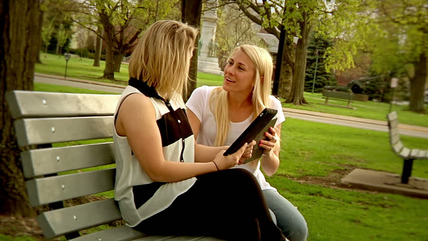 Two young women enjoy using their tablet PCs in the park.