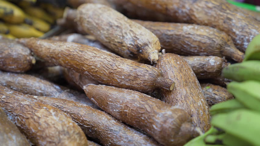 A pile of fresh cassava roots displayed on a market stall, showcasing their rough texture and natural appeal in a food market setting.